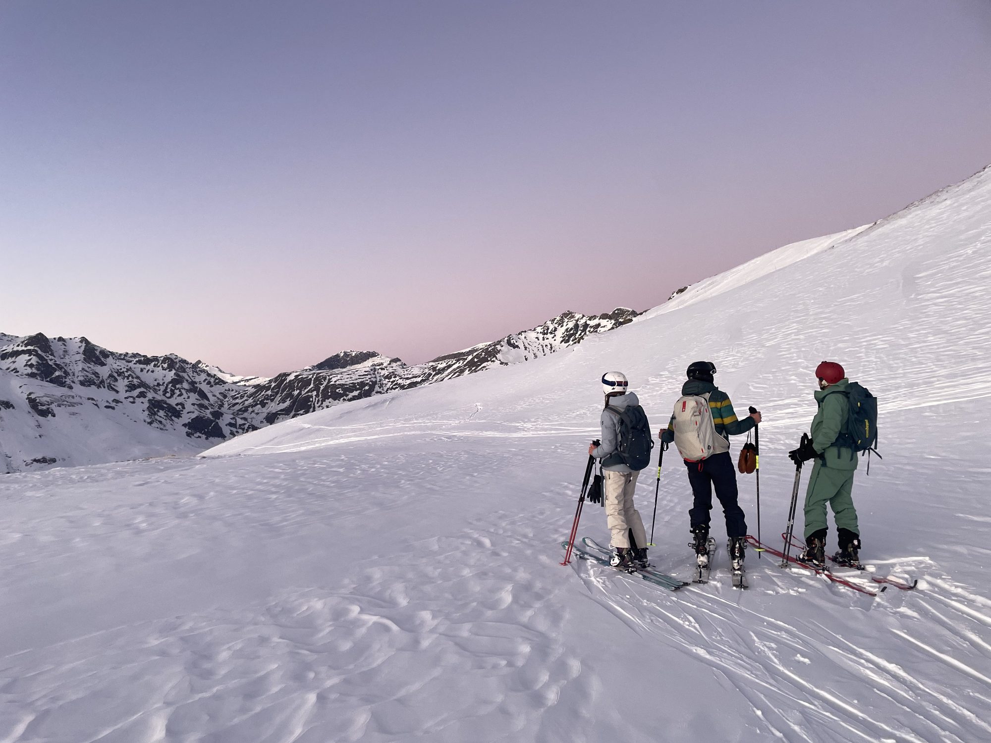 Trois skieurs contemplant les montagnes au lever du jour