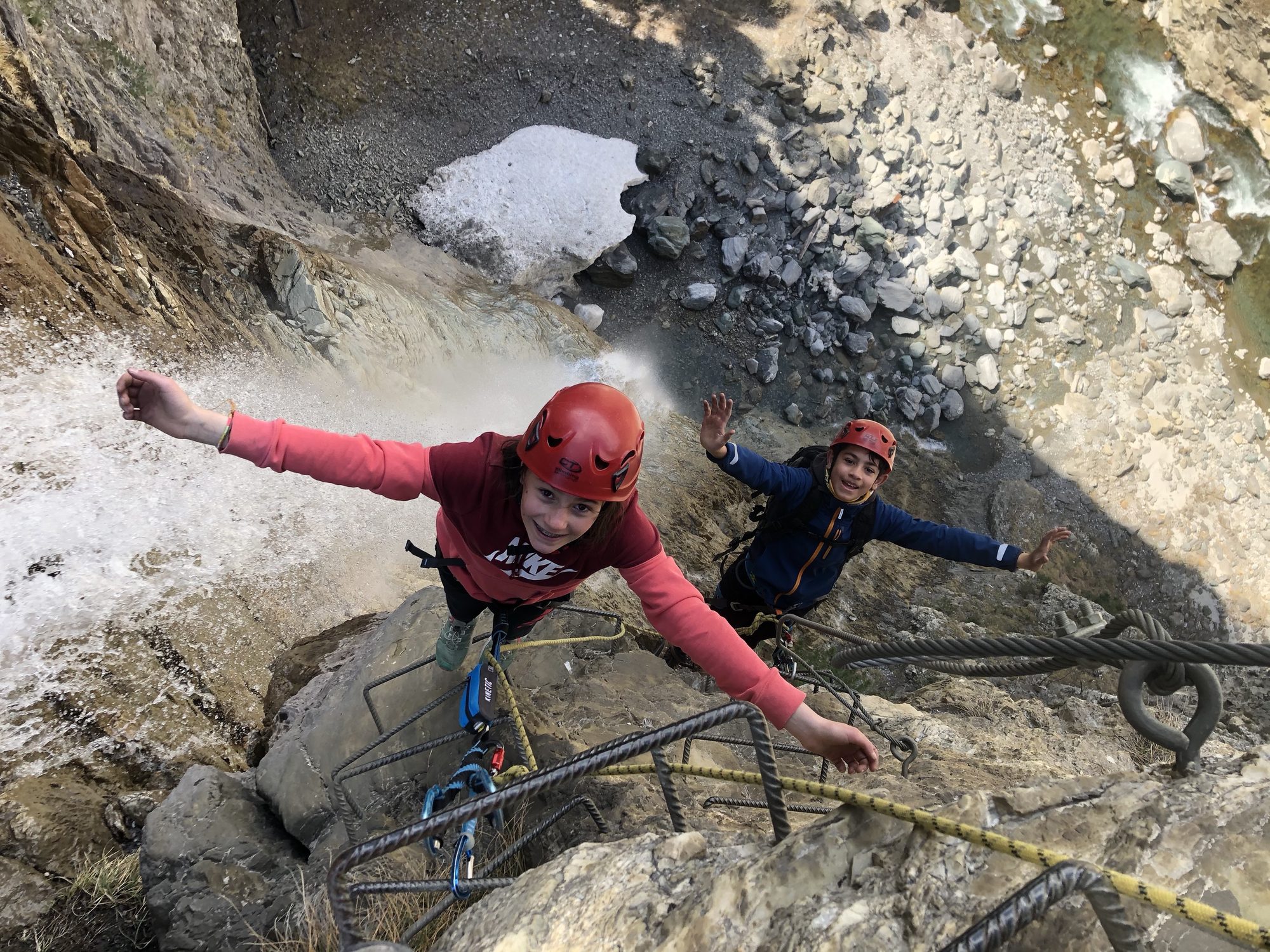 Enfants tout sourire près d'une cascade, bras en l'air